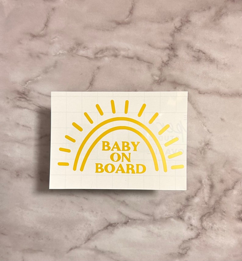 May include: Gold vinyl sticker with a sun design and the text "BABY ON BOARD".