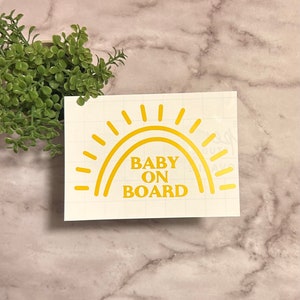 May include: A yellow sun with rays and a rainbow arch with the text "BABY ON BOARD" on a white background.