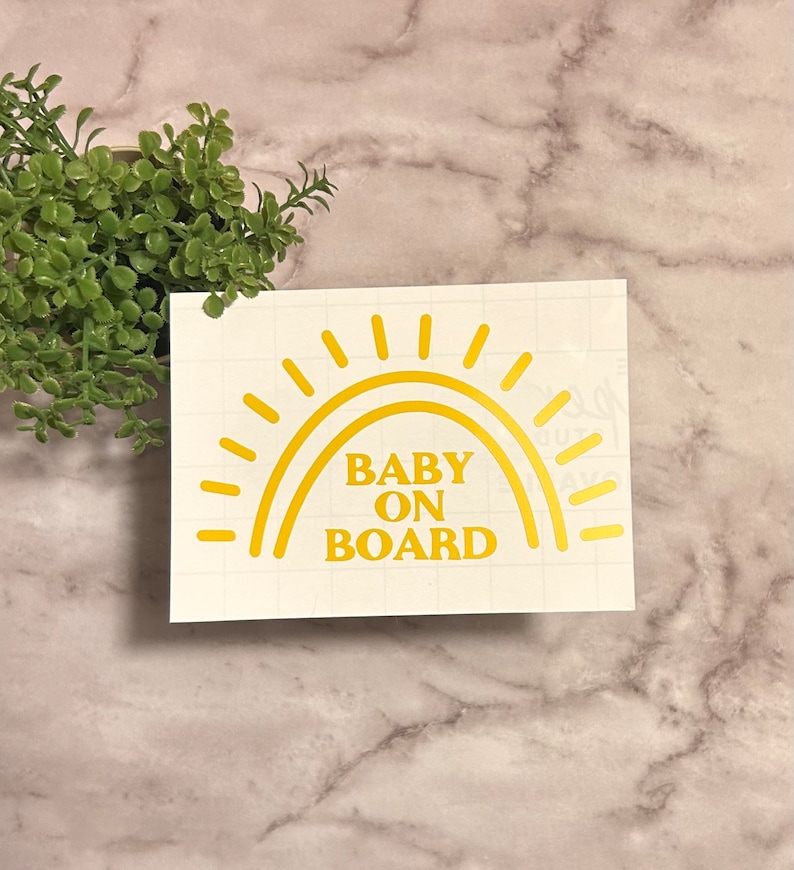 May include: A yellow sun with rays and a rainbow arch with the text "BABY ON BOARD" on a white background.