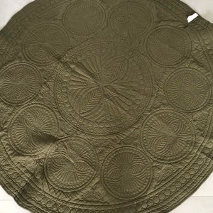 May include: Olive green, round quilted textile with intricate stitched circular patterns. The design features various sizes of circles with detailed internal designs, creating a textured surface. The edges are scalloped.
