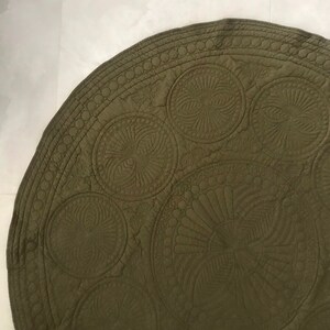 May include: Olive green, circular quilted fabric with intricate stitched circular and fan-like patterns. The edge features a repeating circle design. The fabric has a soft, matte finish and appears to be made of cotton or a similar material.