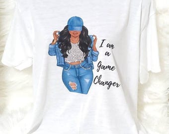 May include: A white short-sleeved t-shirt featuring a graphic illustration of a person wearing a blue baseball cap, a denim jacket, a white top, and blue distressed jeans. The text "I am a Game Changer" is printed in black script next to the figure.