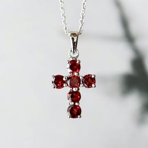 Peut inclure: Un collier en argent avec un pendentif en forme de croix sertie de pierres précieuses rouges. La croix est en argent et comporte sept pierres précieuses rouges.