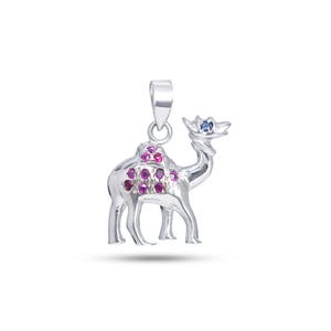 May include: A silver camel pendant with a loop for a chain. The camel has a saddle adorned with pink gemstones and a blue gemstone on its head. The pendant is designed with detailed legs and a curved neck.