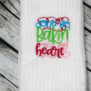 Puede incluir: Toalla de cocina blanca con texto bordado en rojo, rosa, verde y azul que dice "Don't go bakin' on my heart".