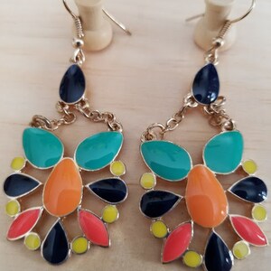 May include: A pair of gold dangle earrings with a multi-colored design. The earrings feature teal, orange, black, red, and yellow enamel accents.