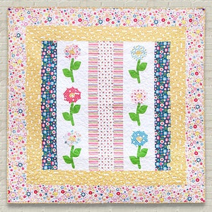 Pu&ograve; includere: Un quilt bianco con un motivo floreale giallo, blu e rosa. Il quilt ha un bordo di piccoli fiori di vari colori.