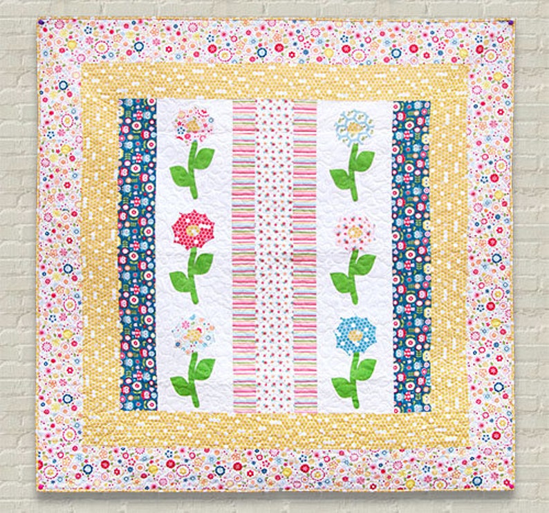 Pu&ograve; includere: Un quilt bianco con un motivo floreale giallo, blu e rosa. Il quilt ha un bordo di piccoli fiori di vari colori.