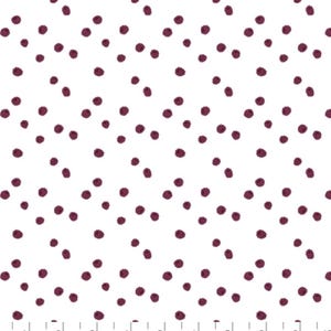 Op de afbeelding: Witte stof met een herhalend patroon van onregelmatig gevormde, donker bordeauxrode stippen. De stippen zijn verspreid over het oppervlak. De stof heeft een liniaal langs de onderrand met de tekst "COTTON + STEEL" en "We make pretty fabrics."