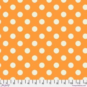 May include: Orange fabric with a repeating pattern of large, cream-colored polka dots. The fabric has a ruler along the bottom edge, marked in inches. The words "Free Spirit" and "freespiritfabrics.com" are also visible.
