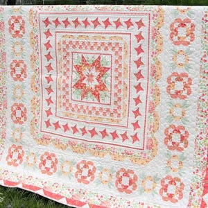 May include: A handmade quilt with a central star design in shades of coral, peach, and green. The quilt features a square pattern with star and floral motifs, bordered by a scalloped edge. The overall design is a mix of geometric and floral patterns.