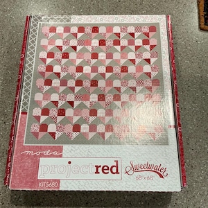 May include: A boxed quilt kit featuring a heart-patterned design in shades of red and white on a gray background. The box is labeled "projectred Sweetwater" and measures 68" x 68". The kit includes the fabric pieces needed to create the quilt.