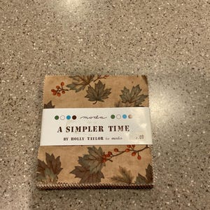 May include: A stack of fabric squares with a fall-themed leaf and berry pattern. The fabric is tan with brown and green leaves and red berries. A white label reads "A Simpler Time" by Holly Taylor for Moda.
