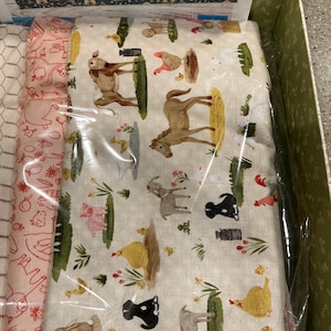 May include: A collection of folded fabric pieces featuring farm-themed prints. One piece displays a cream background with illustrations of cows, horses, pigs, chickens, and goats. Another piece is light pink with a white line-art farm pattern.