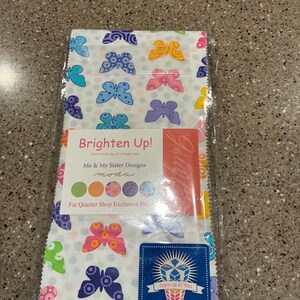 May include: A fabric bundle featuring a white background with colorful butterfly patterns in various shades of blue, pink, yellow, and green. The package includes a label that reads "Brighten Up!" and "Me & My Sister Designs".