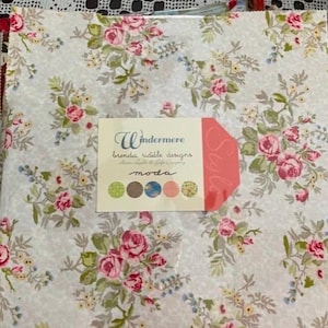 May include: A stack of fabric squares with a floral pattern featuring pink roses, green leaves, and small yellow flowers on a light gray background. A tag reads "Windermere Brenda Riddle Designs moda".