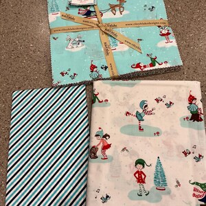 May include: A stack of Christmas-themed fabric squares tied with a ribbon, featuring elves, reindeer, and winter scenes. Additional fabric pieces include a blue and white striped pattern and a white fabric with elf illustrations.