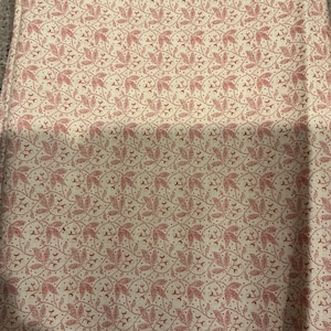 May include: A piece of cream-colored fabric featuring a repeating pattern of small, red, stippled leaf and vine motifs. The white selvage edge displays the printed text: Presents "FARMHOUSE LIVING" c.1830 by Jeanne Horton.