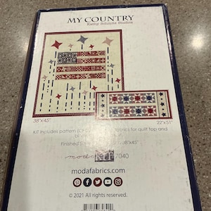 May include: A box for a quilting kit with a patriotic theme. The design features a stylized American flag and stars in red, white, and blue. The finished size is 38" x 45". The kit includes a pattern and fabrics.