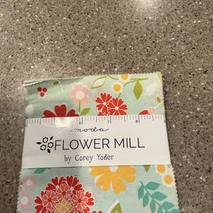 May include: A stack of fabric squares with a floral pattern in red, pink, yellow, and green on a light blue background. The label reads "FLOWER MILL by Corey Yoder."