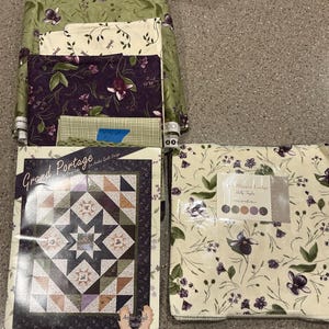 May include: A collection of fabric bundles and quilt patterns. The fabrics feature floral and botanical designs in shades of green, purple, and cream. The quilt pattern titled "Grand Portage" is visible, along with a pattern labeled "Slipper Lodge".