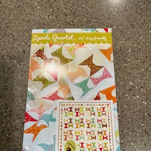 May include: A quilt pattern titled "Spools Quartet" with a colorful design of bow tie shapes. The pattern is "2 1/2" strip friendly" and includes a smaller image of the finished quilt. The Fig Tree & Co. logo is visible.