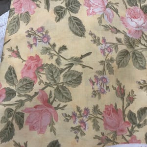 May include: A yellow fabric featuring a floral pattern with pink roses, small purple flowers, and green leaves. The white selvage edge displays the text Moondance by Robyn Pandolph for Moda and the website address www.modafabrics.com.