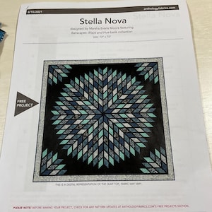 May include: A printed pattern for a quilt titled "Stella Nova" by Marsha Evans Moore. The design features a central starburst pattern in shades of blue, teal, and gray on a black background. The quilt size is 72" x 72".