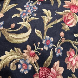 May include: A black fabric featuring a floral pattern with pink, red, and blue flowers, along with green and tan leaves. The selvage edge includes the text "Howard and Patek for moda" and "modafabrics.com Pattern # 2000" printed in black.