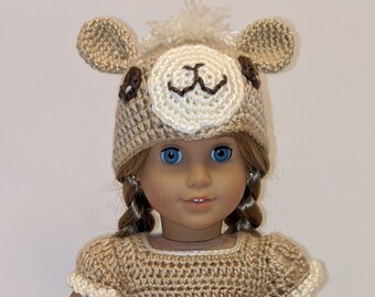 May include: A crocheted llama costume for an 18-inch doll, featuring a brown and white llama hat with ears, a brown dress with a flower trim, and white leggings.
