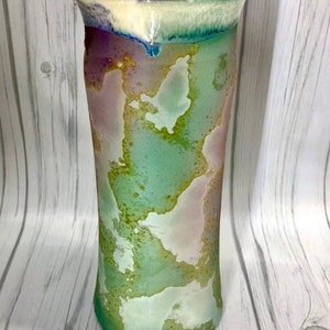 May include: A tall, cylindrical ceramic vase with a white, green and purple glaze. The glaze has a mottled, abstract pattern.