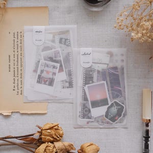 May include: Two clear plastic envelopes filled with decorative stickers. The envelopes are labeled "music" and "celestial". The stickers feature a variety of designs, including film strips, photos, and abstract patterns.