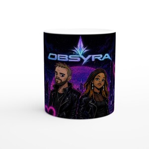 Op de afbeelding: Witte keramische mok met een levendige illustratie. Het ontwerp toont het woord "OBSYRA" in blauw en paars, twee figuren, een man en een vrouw, tegen een stadsgezicht met een paarse planeet en een kristal.