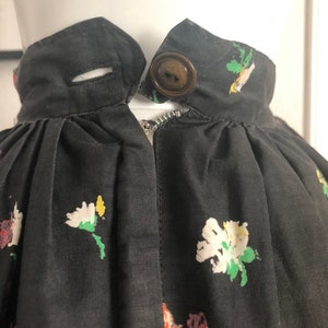 May include: A black skirt featuring a floral print with white, yellow, and red flowers. The waistband includes a single brown button closure, a horizontal buttonhole, and a metal zipper located directly below the waistband center.