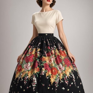May include: A dress featuring a cream-colored short-sleeved bodice with a boat neckline and a high-waisted, full-length black skirt. The skirt is decorated with a vibrant, multi-colored floral print in shades of red, yellow, and green.