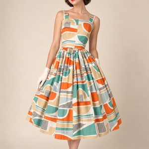 May include: A sleeveless dress featuring a square neckline and a full, pleated skirt. The fabric displays a geometric pattern with repeating shapes in shades of orange, teal, light blue, and black lines against a cream-coloured background.
