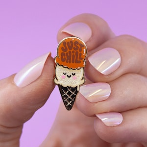 May include: Gold enamel pin shaped like an ice cream cone with a smiling face and the words "Just Chill" on the ice cream.