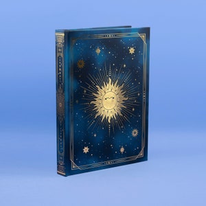 Può includere: Un diario con copertina rigida con un design celeste. La copertina è blu scuro con un motivo dorato di sole e stelle. Il dorso e i bordi sono anch'essi adornati con dettagli dorati, creando un'estetica mistica.