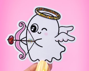 May include: A white ghost with a halo, wings, and a pink bow and arrow. The ghost has a winking face and a pink heart on the arrow.