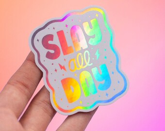 以下が含まれることがあります： カラフルなバブルレターで「SLAY all DAY」というフレーズが書かれたホログラフィックステッカー。ステッカーは雲のような波状のボーダーで、小さな星と稲妻のグラフィックが特徴です。背景はピンクとオレンジのグラデーションです。