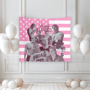 May include: A pink and white tapestry featuring a collage of images of men, with the text "Daddy Di Laurentis" in cursive. The background is a pink American flag design. White balloons are in the foreground.