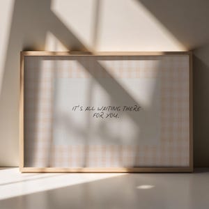 May include: A framed print with a light wood frame. The print has a soft, checkered background with the handwritten text, "IT'S ALL WAITING THERE FOR YOU." The artwork is displayed on a white surface with shadows.
