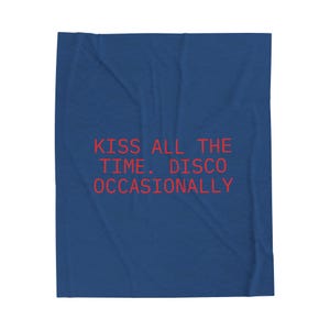 May include: A blue blanket with the red text "KISS ALL THE TIME. DISCO OCCASIONALLY." The blanket is folded and has a soft, textured appearance. The text is in a bold, sans-serif font.
