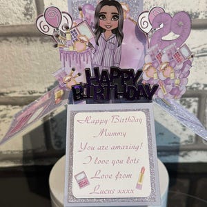May include: A purple and white pop-up card with a cartoon woman wearing pyjamas and makeup. The card says "Happy Birthday Mummy You are amazing! I love you lots Love from Lucus xxxx".