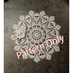 May include: Cream-colored, crocheted doily featuring a skull pattern. The doily has a circular design with skull motifs around the edge. The words "Pattern Only" are printed on the image. A small, white, skeletal hand holds a round tag.