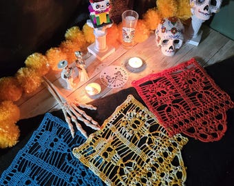 Puede incluir: Tres paneles rectangulares de ganchillo con intrincados patrones de calaveras en azul, amarillo y rojo. El panel azul está a la izquierda, el amarillo en el centro y el rojo a la derecha. Cada pieza muestra un diseño calado detallado.