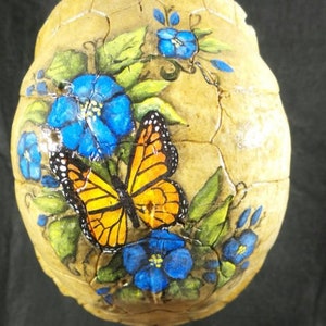 May include: A painted turtle shell with a monarch butterfly and blue flowers. The shell is cracked and has a natural brown color.