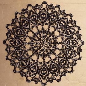 May include: Black crochet doily with a skull design. The doily is circular and has a delicate lace pattern.