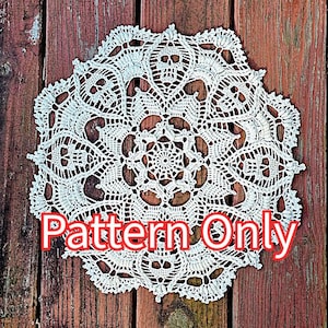 Puede incluir: Un tapete blanco de ganchillo con un diseño circular detallado. El tapete presenta un intrincado patrón de calados y elementos texturizados. El texto "Pattern Only" está superpuesto en la imagen con letras rojas. El tapete está sobre un fondo de madera rústica.