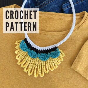 May include: A crocheted necklace with a white, black, and teal design. The necklace has a fringe of yellow yarn.
